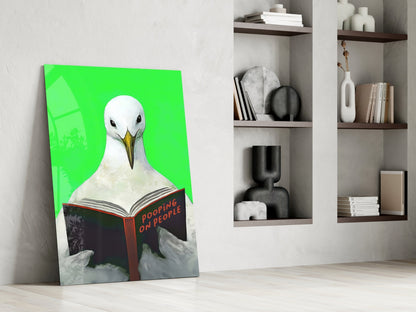Glass wall art canvas leaning against white wall displays white seagull reading "Pooping on People" book on bright green background.