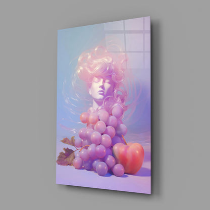 Angled view of glass wall art featuring a serene face with pink hair surrounded by glowing purple grapes and a red apple against a gradient blue-to-purple background.