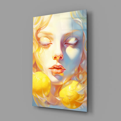 A glass wall art panel displaying a portrait of a woman's face with closed eyes, rendered in warm yellows and cool blues, mounted at an angle against a gray background.