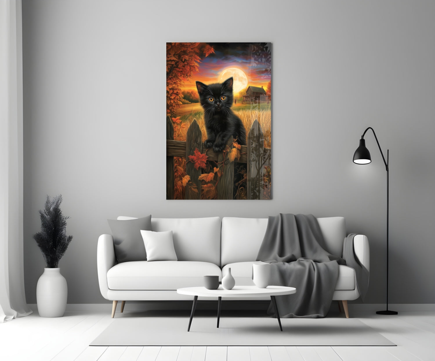 Glass wall art depicting a black cat with glowing eyes before an autumn sunset landscape, displayed above a white sofa in a modern living room.