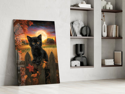 Black cat with golden eyes facing forward against autumn sunset landscape with full moon, displayed as glass art leaning against white wall beside shelving.