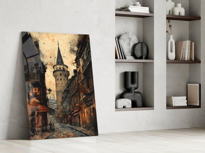 Glass wall art leaning against white wall displays warm-toned street scene with historic tower, alongside styled shelving unit with decorative objects and books.