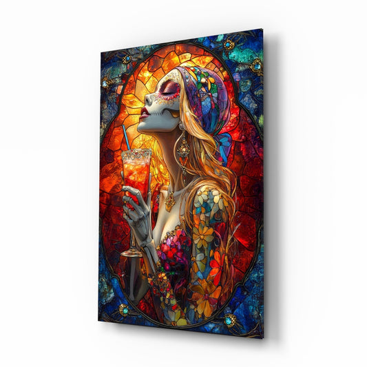 Glass wall art panel displayed at an angle showing a stained glass-style illustration of a skeletal figure with flowing hair holding a cocktail glass, featuring vibrant reds, blues, oranges, and gold tones.