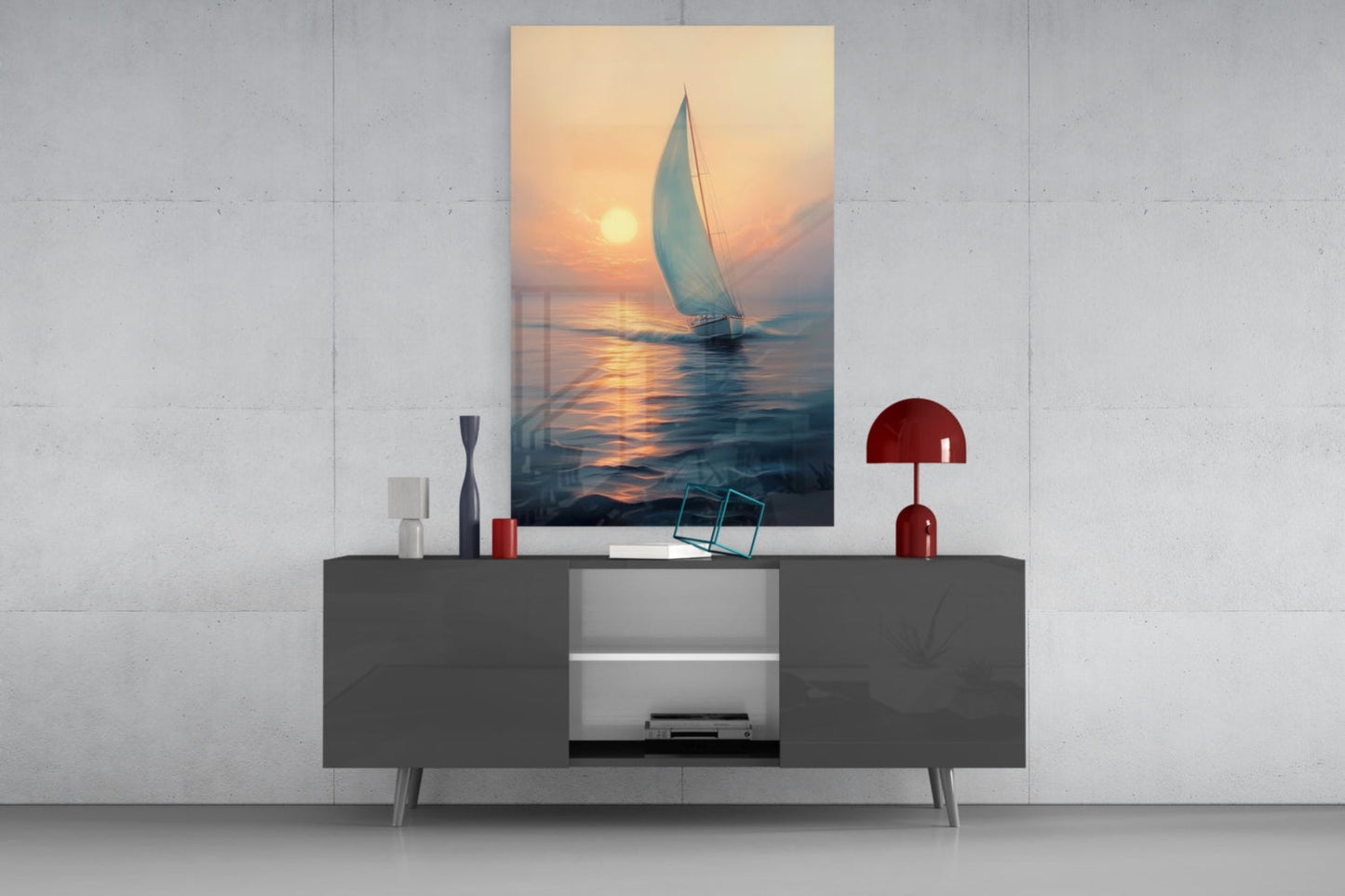 Vertical glass wall art displaying a sailboat at sunset mounted above a gray console table with red decorative lamp and accessories.