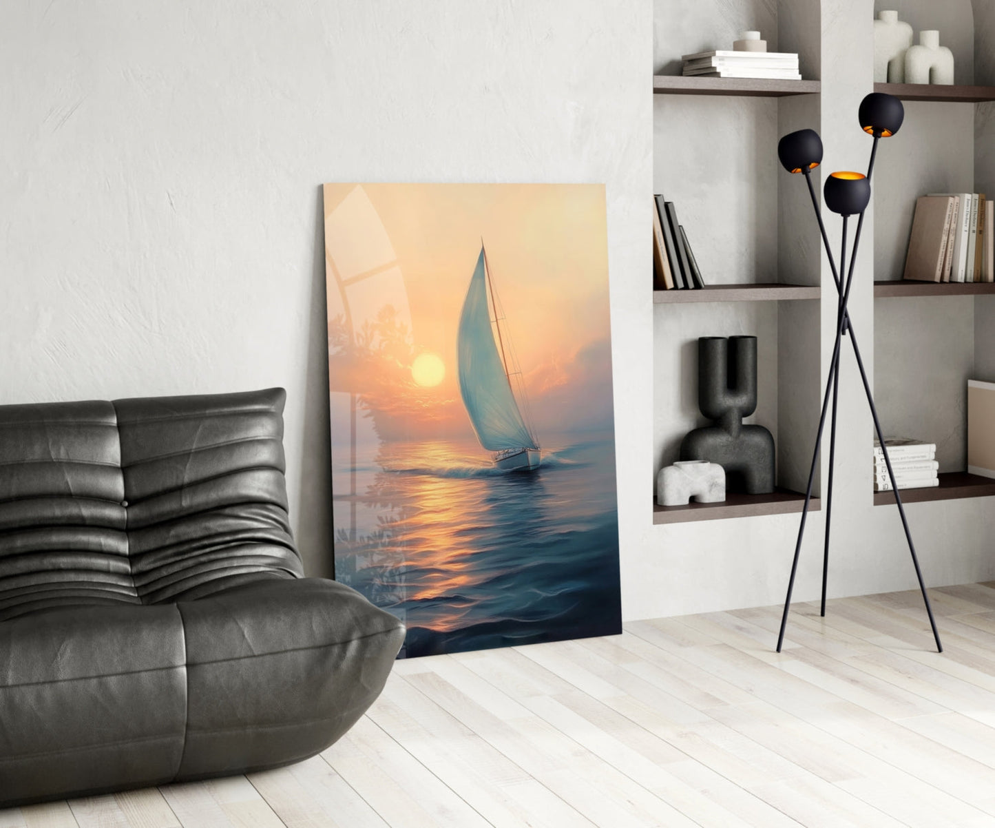Sunset sailboat glass wall art leaning against white wall in modern living room with gray leather sofa and shelving.