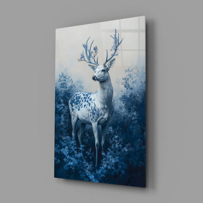 Angled view of glass wall art featuring a white deer with blue antlers surrounded by blue foliage on gradient background.
