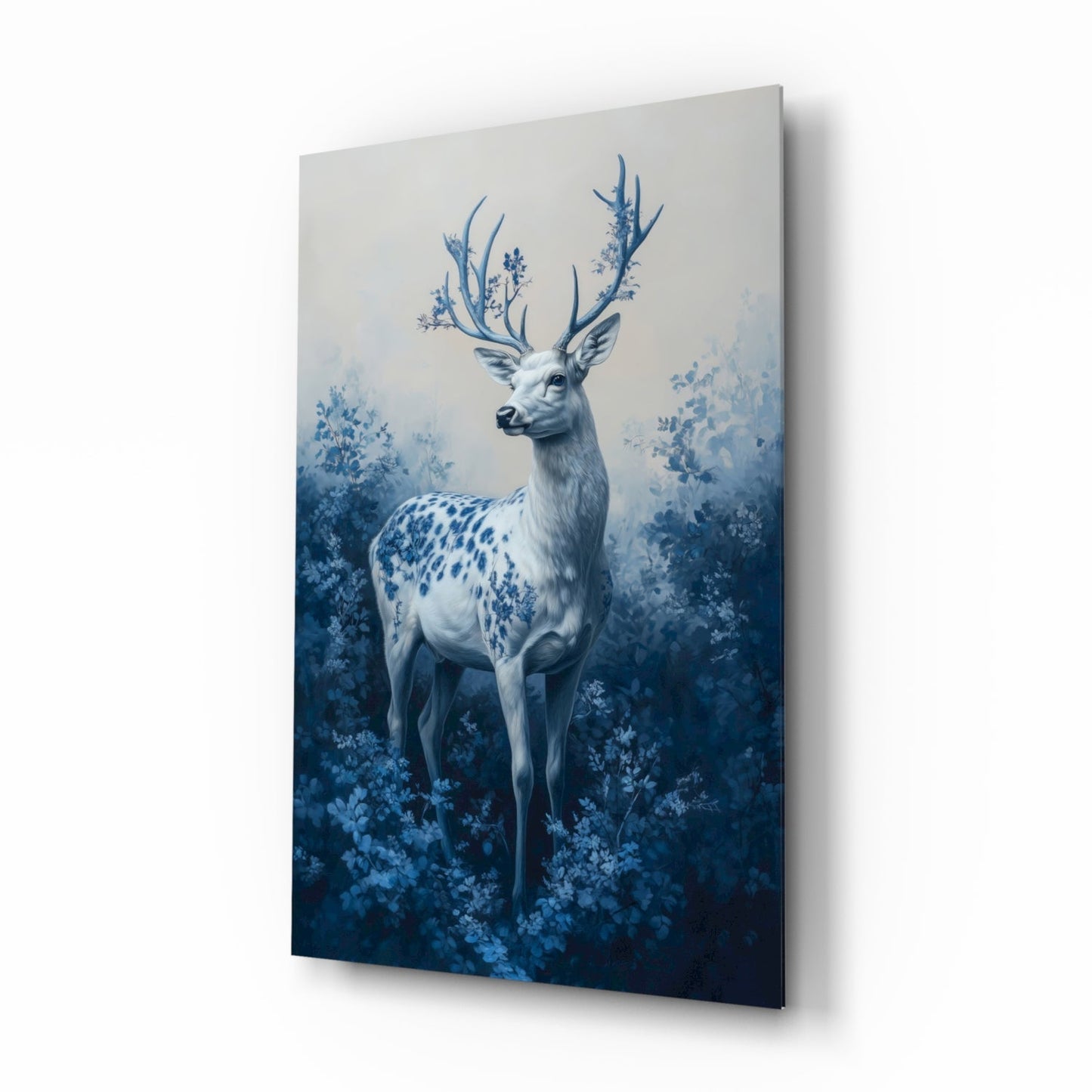 Angled perspective of glass wall art displaying a white deer with blue antlers surrounded by blue foliage against gradient blue background.
