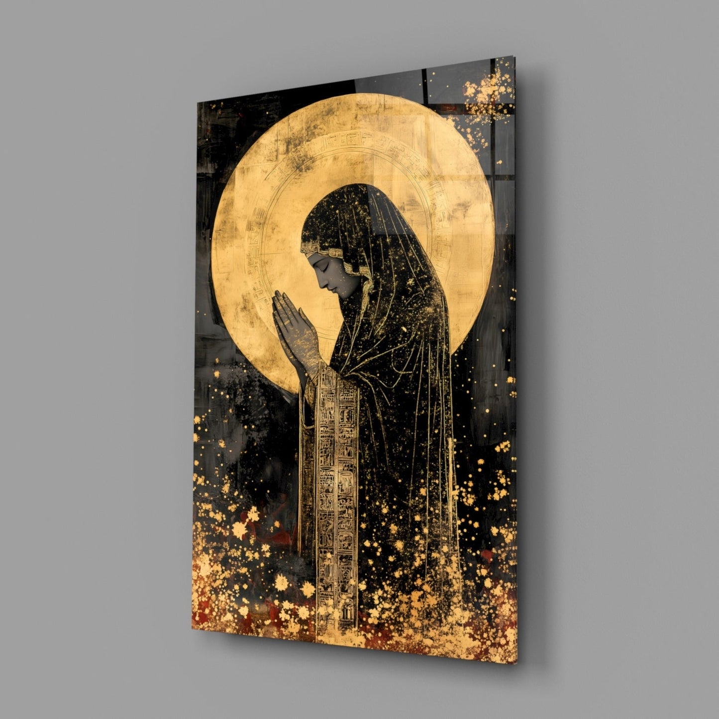 Angled view of glass wall art depicting a praying figure in profile with golden halo and Egyptian hieroglyphic robes against black background with gold particle effects.
