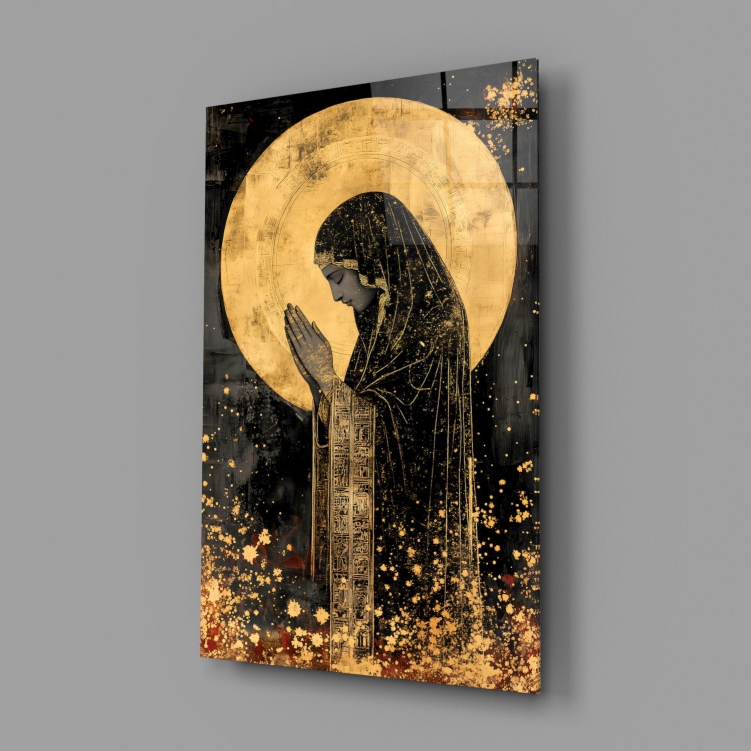 Angled view of glass wall art depicting a praying figure in profile with golden halo and Egyptian hieroglyphic robes against black background with gold particle effects.