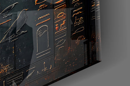 Close-up angled view of black glass panels with gold-etched winged figures and hieroglyphic designs, backlit to highlight relief details.