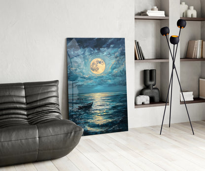 Glass wall art depicting a full golden moon over a nighttime ocean with a small boat, displayed in a modern living room beside a black leather chair.