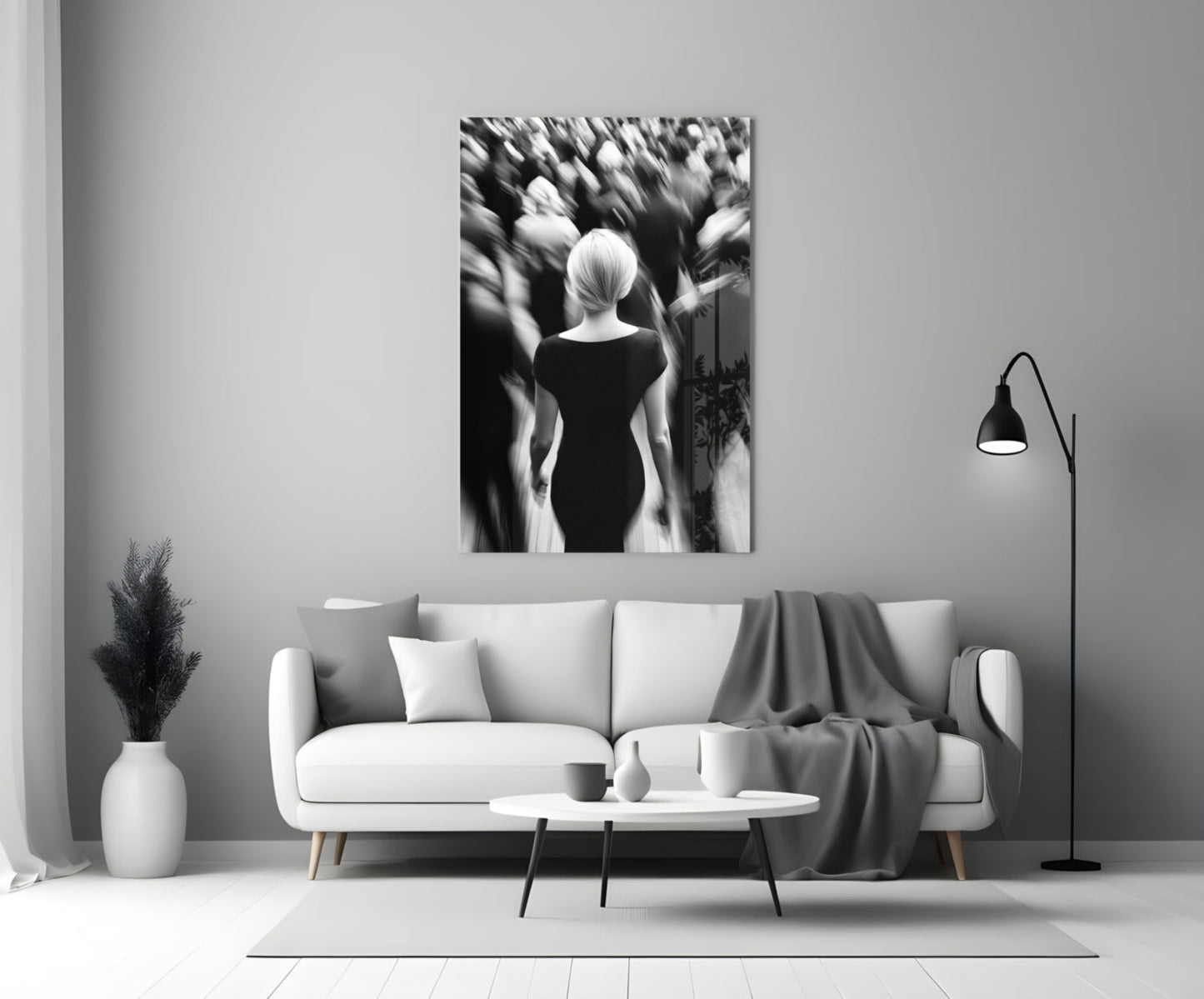 Black and white glass wall art depicting a solitary figure viewed from behind amid a blurred crowd, displayed above a white sofa in a minimalist living room setting.