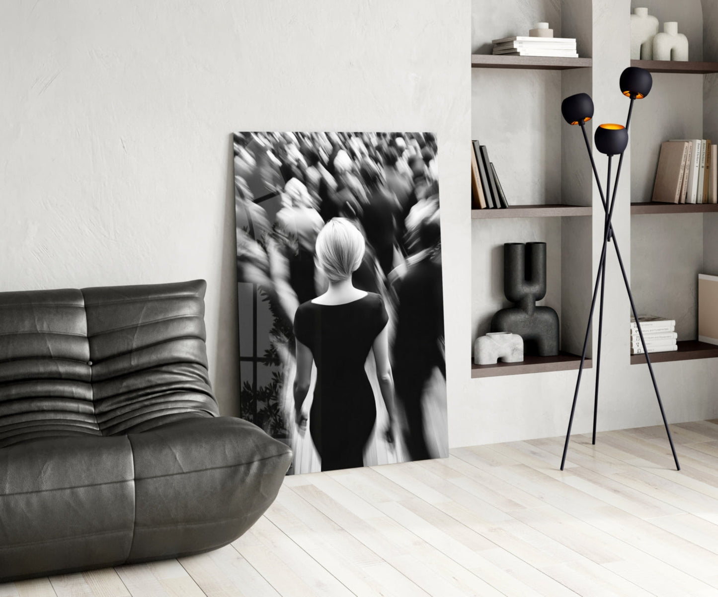 Black and white glass wall art depicting a solitary figure viewed from behind surrounded by blurred crowd, displayed in modern living room with leather sofa and shelving.