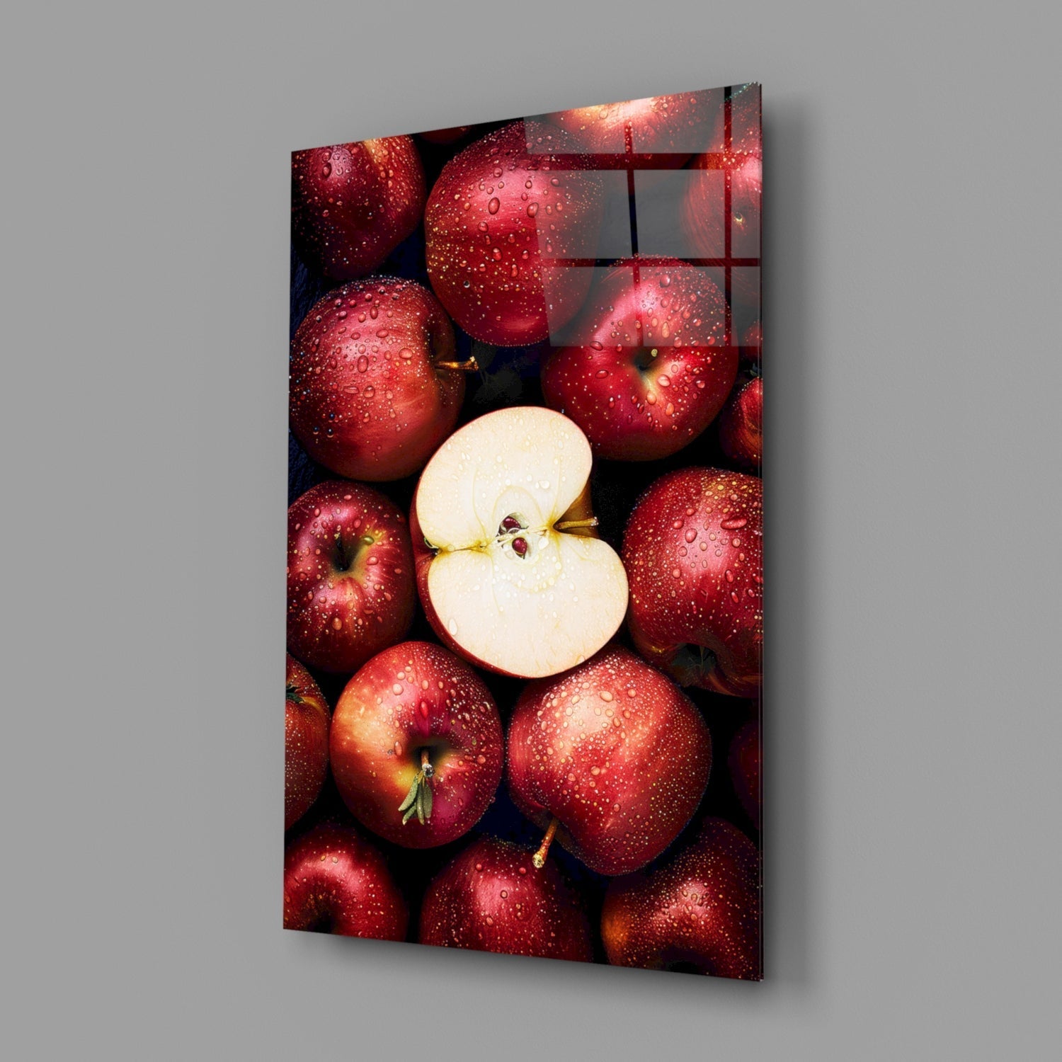 Glass wall art panel displaying fresh red apples with water droplets surrounding a sliced apple half, angled perspective view.