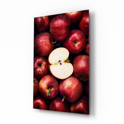 Red apples with water droplets surrounding one sliced apple half, displayed on glass wall art with dark background.