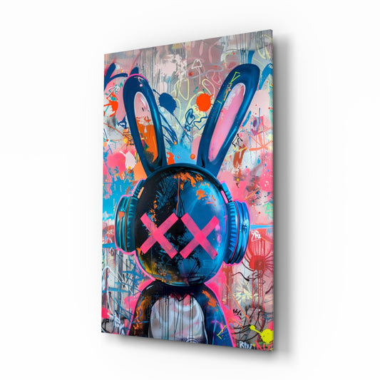 Angled three-quarter view of glass wall art featuring a stylized rabbit head with blue headphones and pink X eyes against a vibrant multicolored graffiti background.