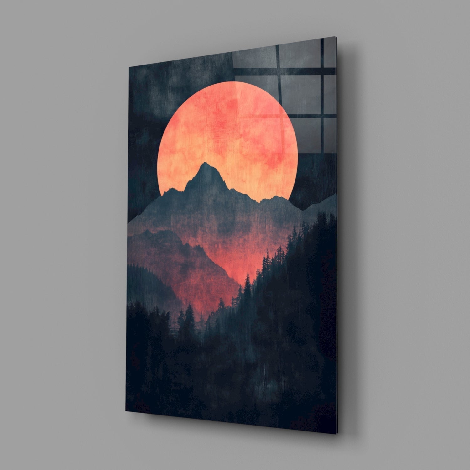 Angled view of glass wall art displaying a large coral sun behind a dark mountain and forest silhouette against a gray wall.