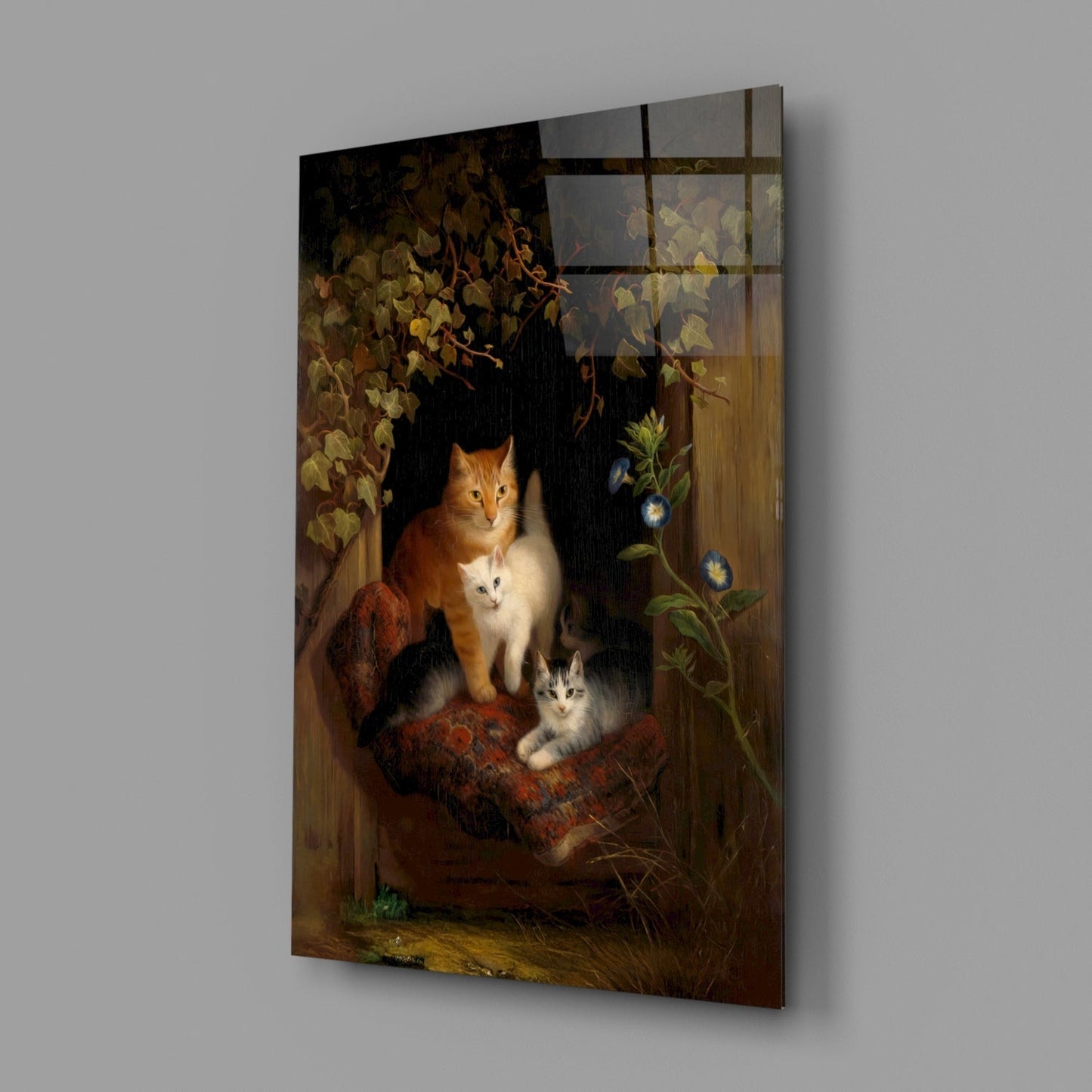 Angled view of glass wall art depicting an orange and white cat with two kittens on a wooden surface, surrounded by autumn foliage and flowering vines against a dark background.