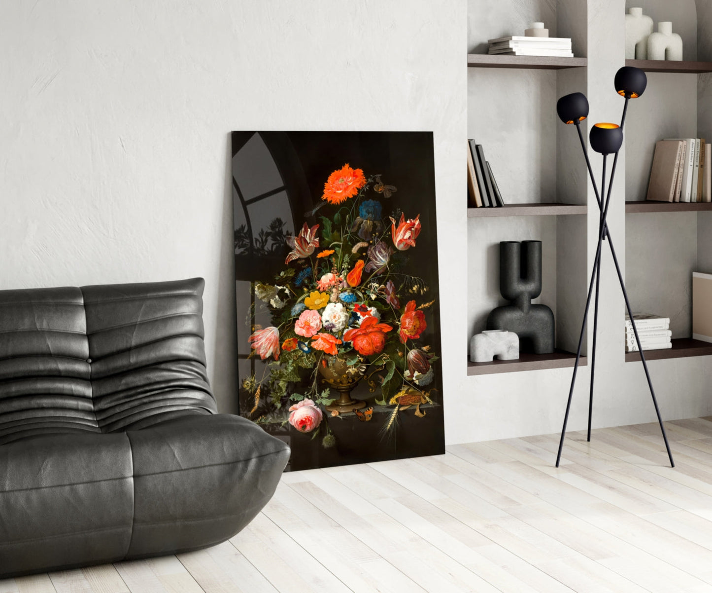 Modern living room interior featuring a vibrant floral still-life glass wall art depicting orange and pink flowers against a dark background, displayed next to a black leather chair and white shelving unit.