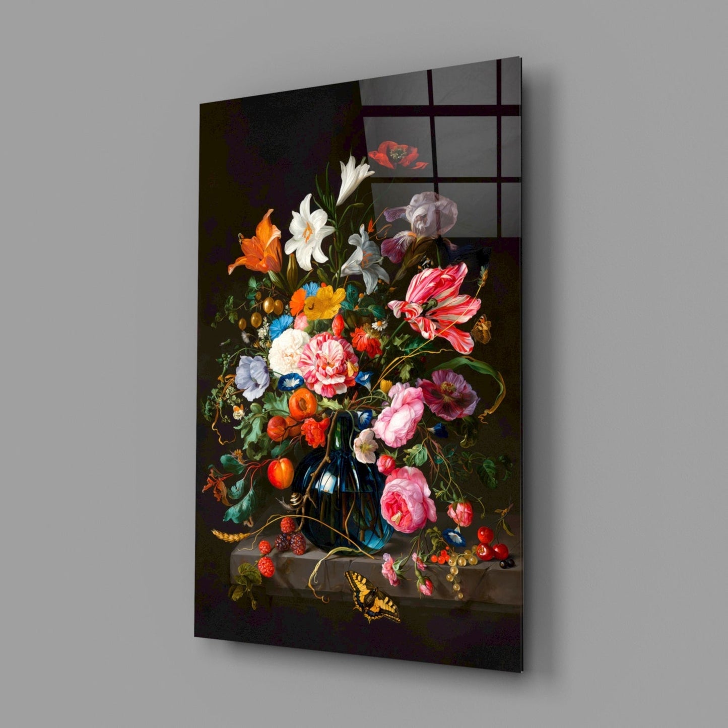 Angled view of glass wall art featuring classical floral still life painting with colorful flowers, blue vase, fruits, and butterfly on dark background.