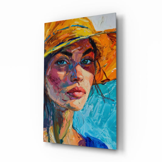 Angled three-quarter view of a glass wall art panel depicting a colorful portrait of a woman wearing an orange hat, with vibrant blue, orange, and turquoise brushstrokes.