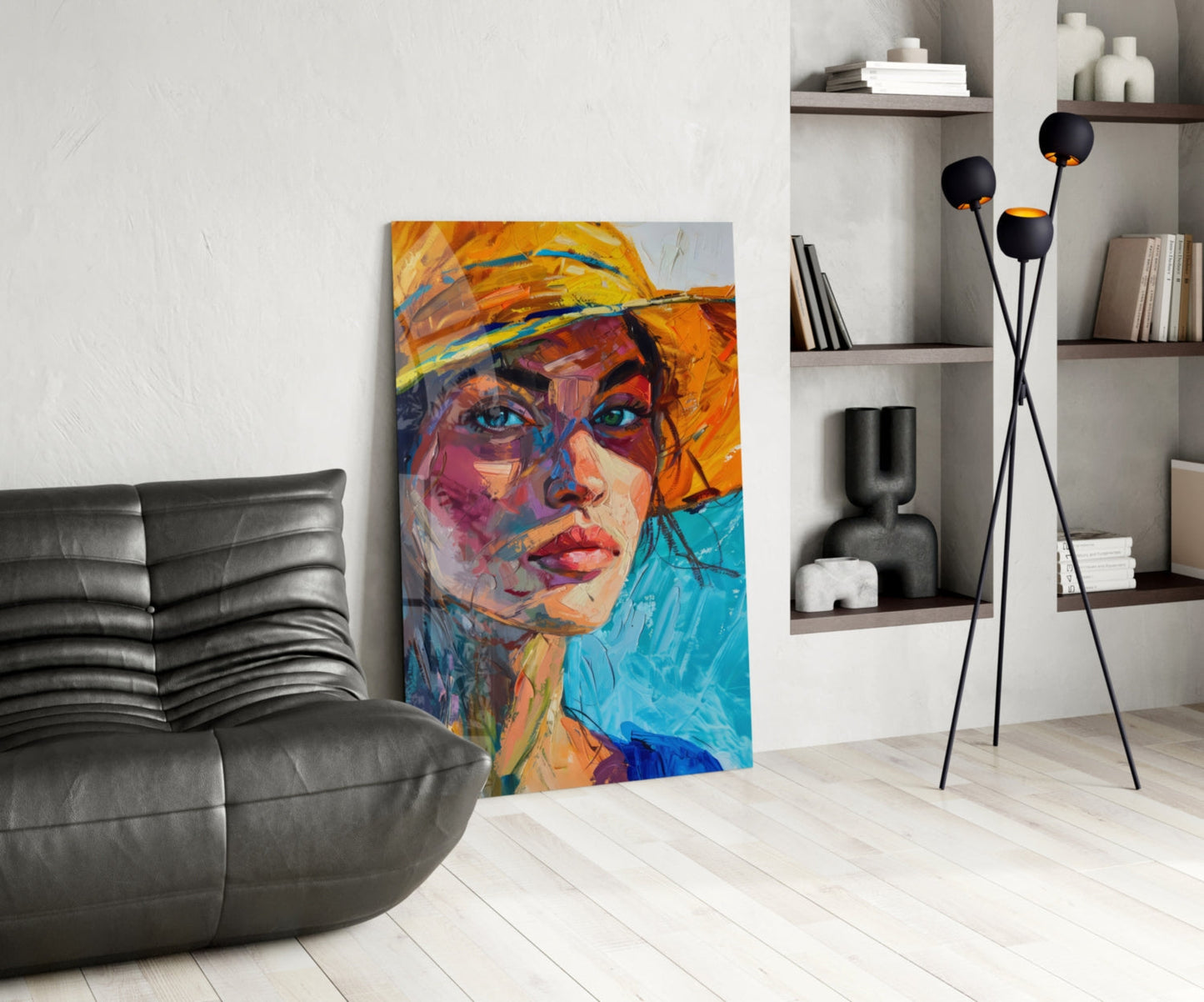 Colorful abstract portrait of woman wearing orange hat displayed as glass wall art in modern living room with black sofa and shelving.
