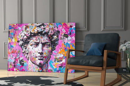 Vibrant graffiti-style glass wall art featuring a classical bust with pink, magenta, and multicolored abstract elements displayed in a modern interior next to a wooden chair.