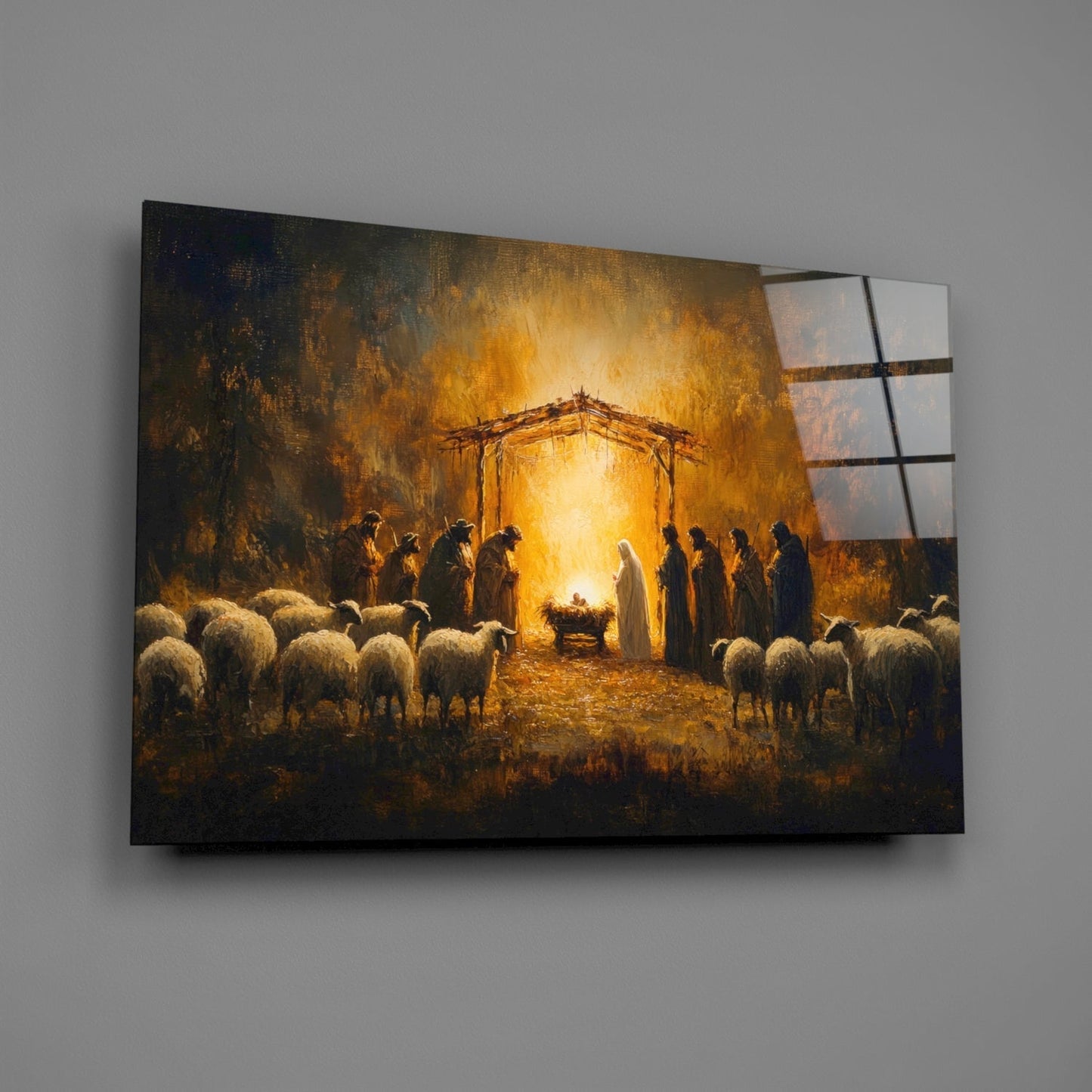 Glass wall art depicting nativity scene with golden light, shepherds, sheep, and manger under wooden structure, displayed at angle against gray wall.