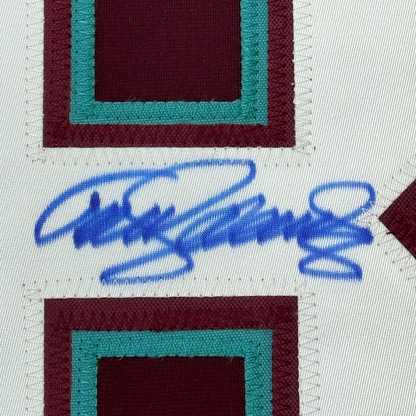 Close-up of blue autographed signature on white fabric between burgundy and teal striped hockey jersey sections.