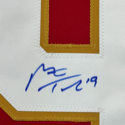 Close-up of blue handwritten signature on white matting with gold and red fabric border framing.