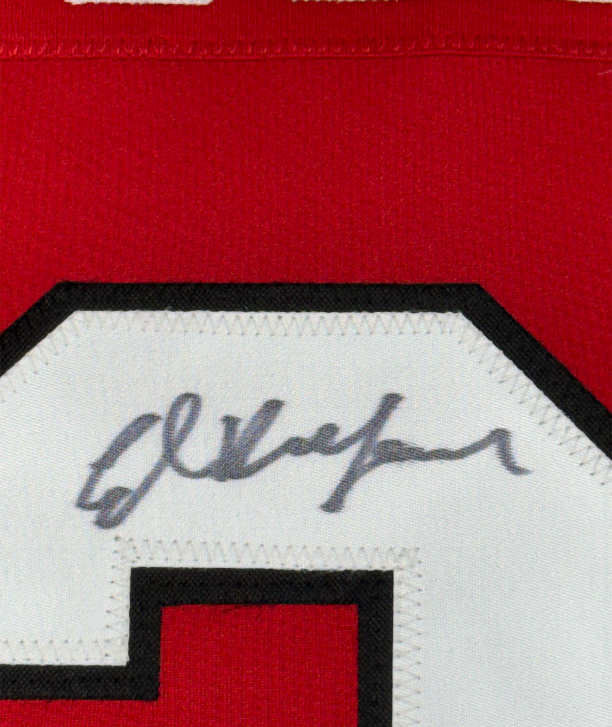 Close-up of handwritten signature on white fabric patch with black border against red jersey material.