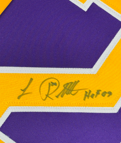 Close-up of autographed yellow stripe on purple and gold Los Angeles hockey jersey showing handwritten signature and "HOF 09" text.