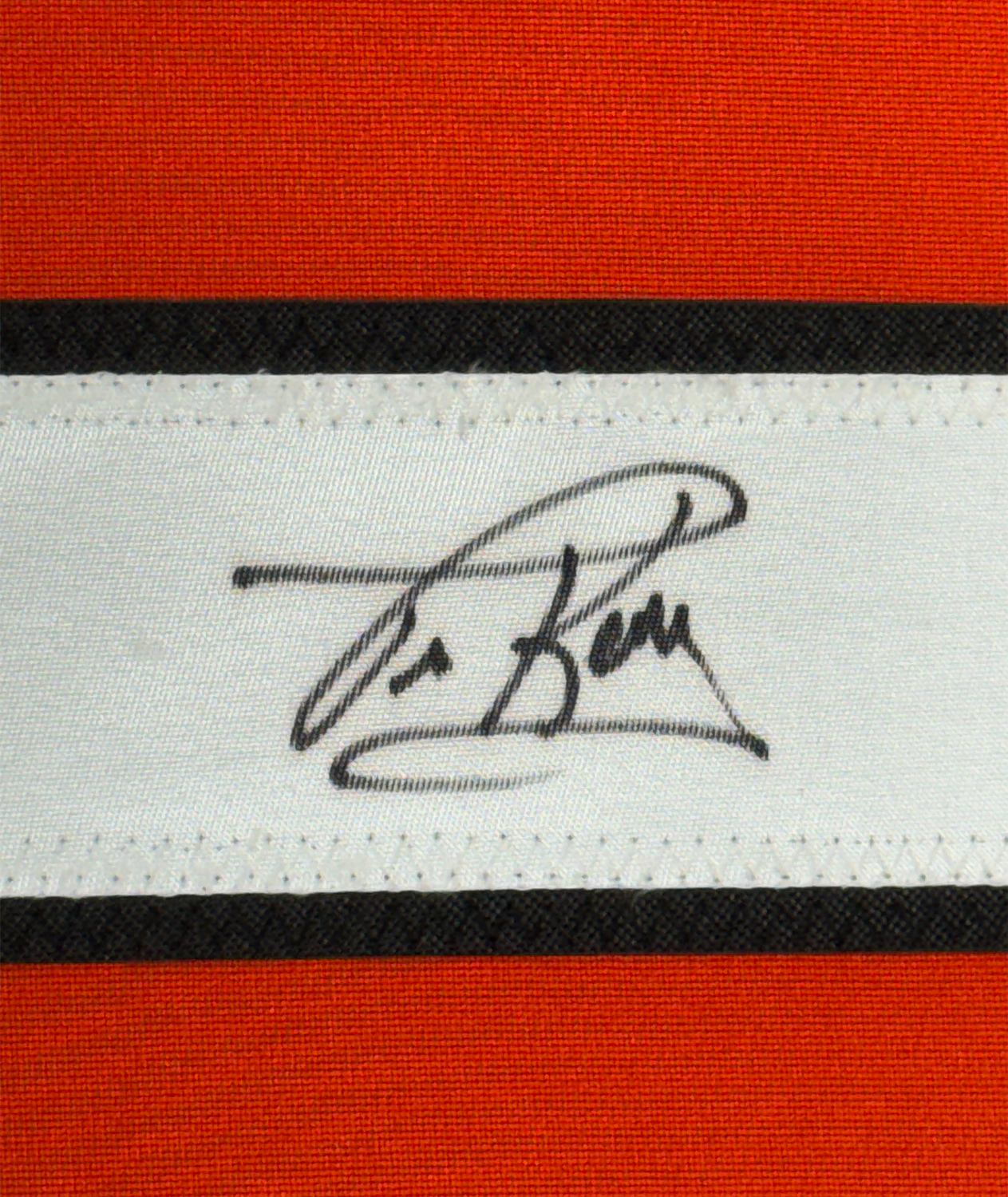 Close-up of handwritten signature in black ink on white fabric strip between red and black horizontal stripes.