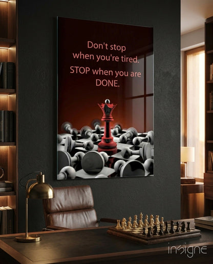 Motivational glass wall art displayed above a desk, featuring a red chess queen among fallen pieces with text "Don't stop when you're tired. STOP when you are DONE.
