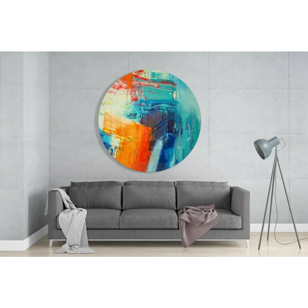 Vibrant circular tempered glass art with bold orange, teal, and blue strokes above gray sofa
