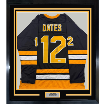 Framed Boston Bruins black hockey jersey number 12 signed by Adam Oates with orange and white stripes, displayed front-facing in black frame with gold matting and nameplate.