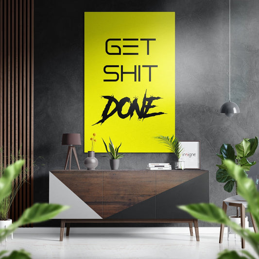 Modern interior room with yellow wall art displaying "GET SHIT DONE" text above wooden console table with plants and decor.