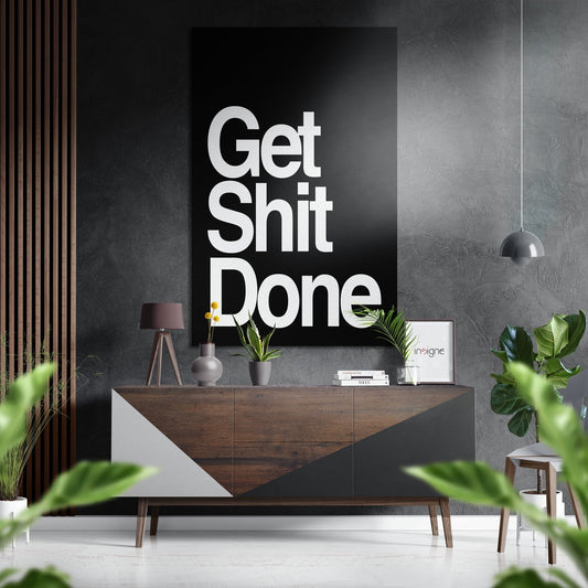 Modern interior with black wall-mounted aluminum sign reading "Get Shit Done" in white text above wooden console table with plants and decor.