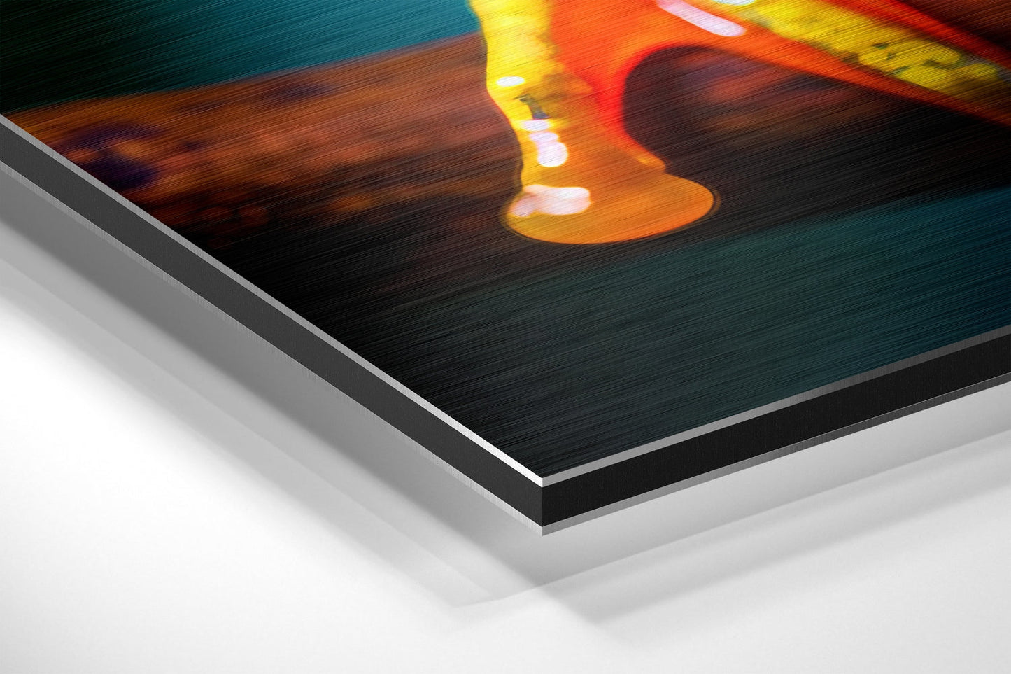 Close-up angled view of brushed aluminum Dibond wall art showing layered edge construction with orange and yellow froglet design on dark teal background.