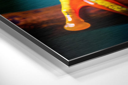 Close-up angled view of brushed aluminum Dibond wall art showing layered edge construction with orange and yellow froglet design on dark teal background.
