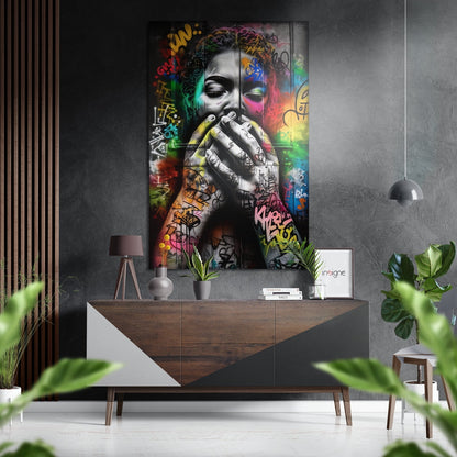 Modern interior featuring colorful street art portrait with graffiti tags on brushed aluminum panel above wooden dresser with plants and pendant lamp.