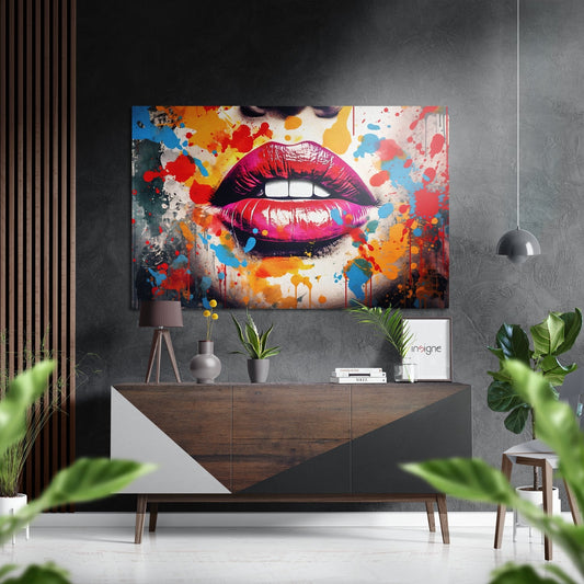 Vibrant pop art lip canvas with red, pink, and multicolored paint splatters hanging above wooden console table in modern interior.
