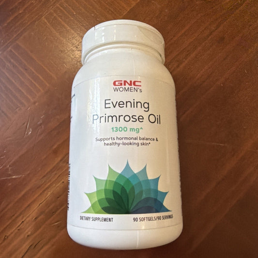 White cylindrical GNC Women's Evening Primrose Oil bottle with green lotus design on wooden surface, front label view.