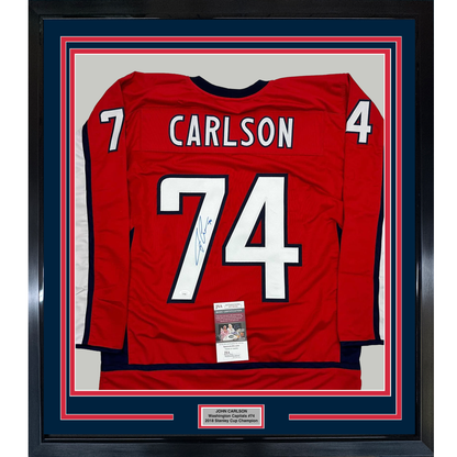 Red Washington Capitals hockey jersey number 74 signed by John Carlson, framed with blue and red matting and JSA authentication certificate visible.