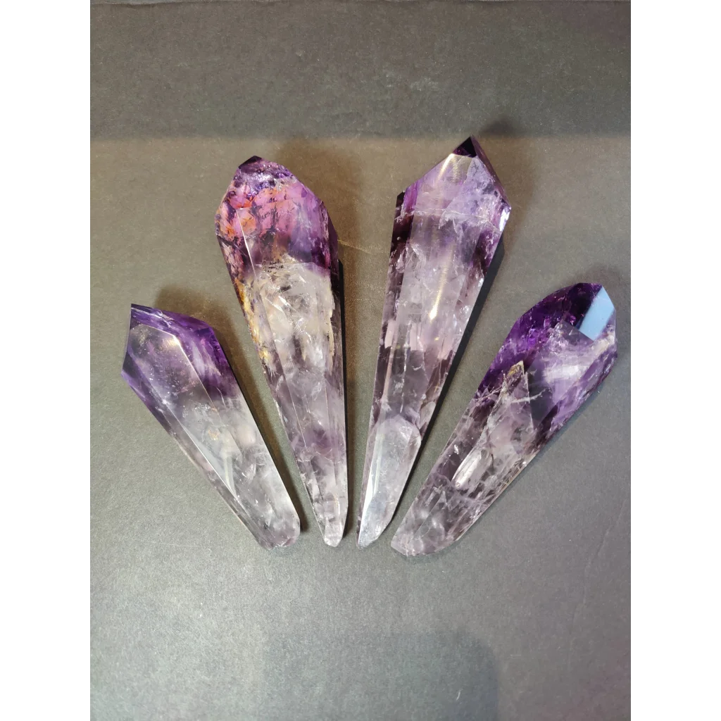 Four amethyst polished scepter wand crystal points with purple to white gradient and natural facets on metal stand