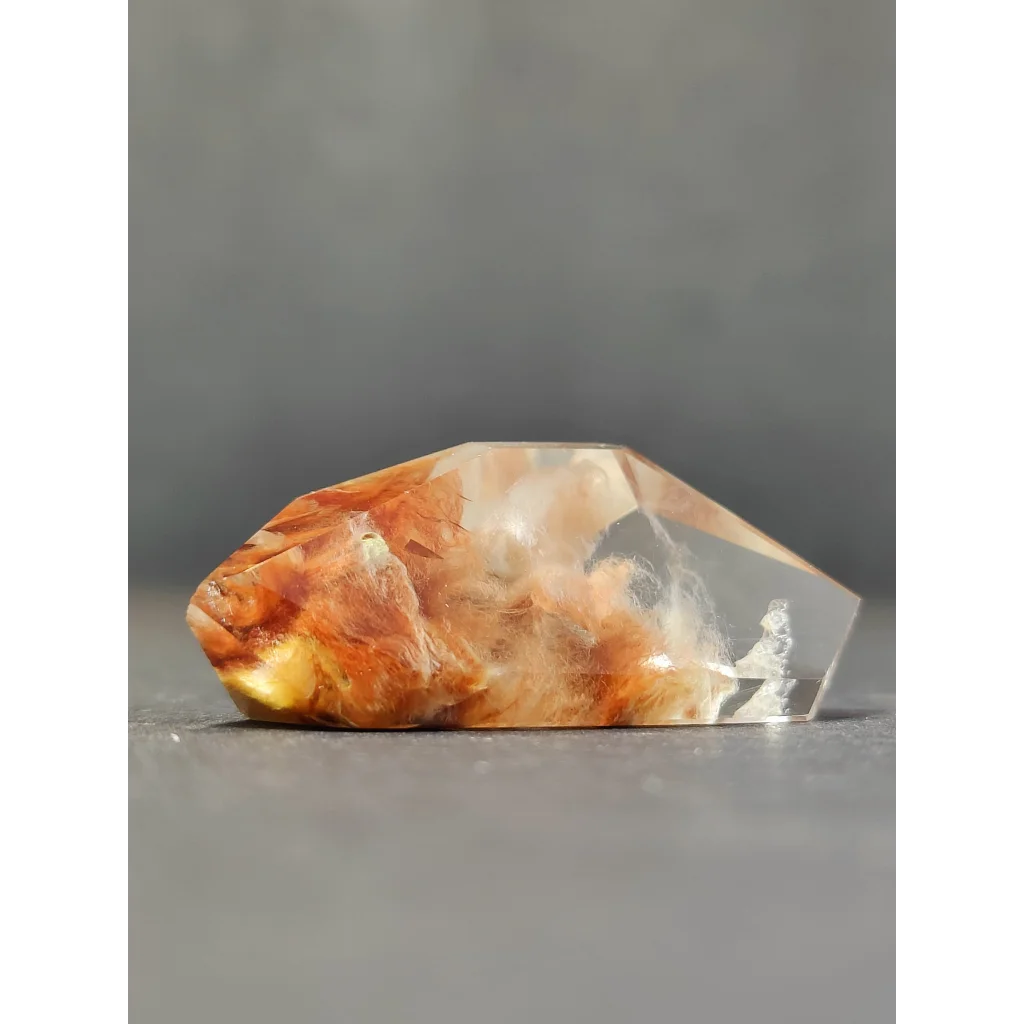 A translucent quartz polished freeform with swirling orange and yellow amphibole angel phantom inclusions
