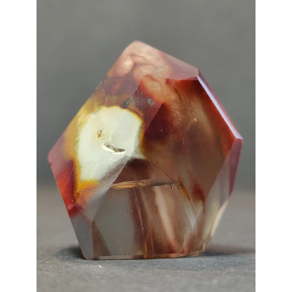 A polished quartz polished freeform amphibole angel phantom with translucent amber and deep red interior streaked by white veins