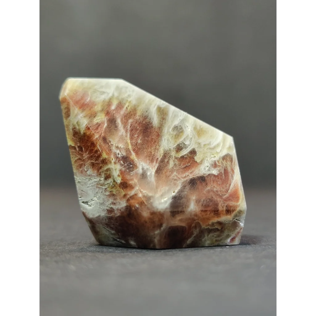 A polished quartz polished freeform featuring irregular red and cream amphibole angel phantom with natural veins