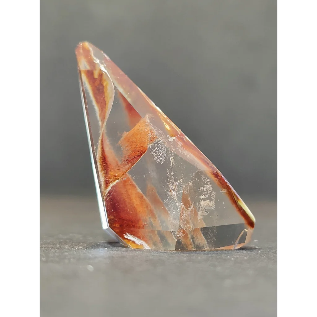 A translucent amber-colored amphibole angel phantom quartz polished freeform with geometric shape and natural inclusions