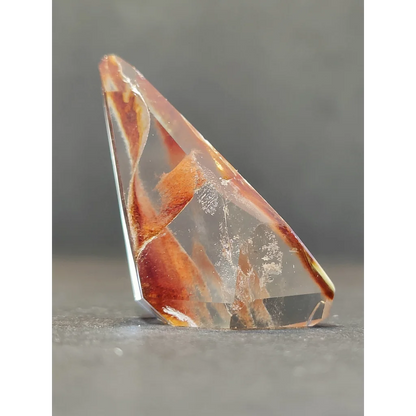 A translucent amber-colored amphibole angel phantom quartz polished freeform with geometric shape and natural inclusions